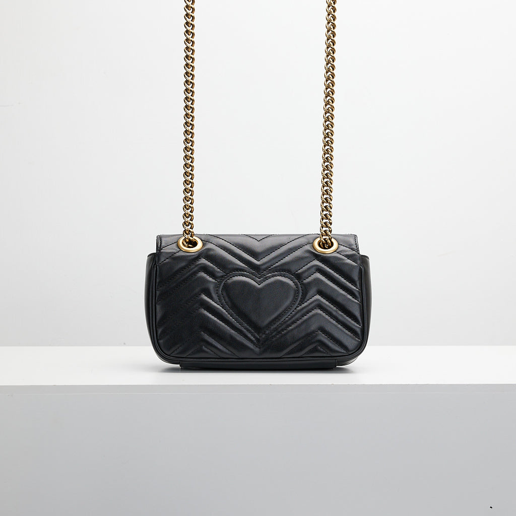 Black quilted handbag gold chain strap on a light gray background