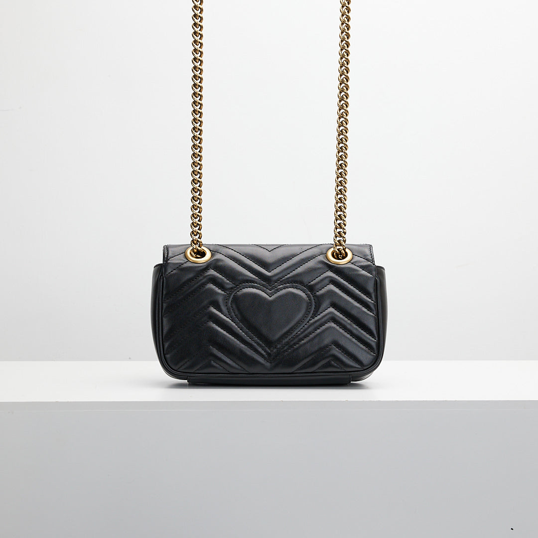 Black quilted handbag gold chain strap on a light gray background