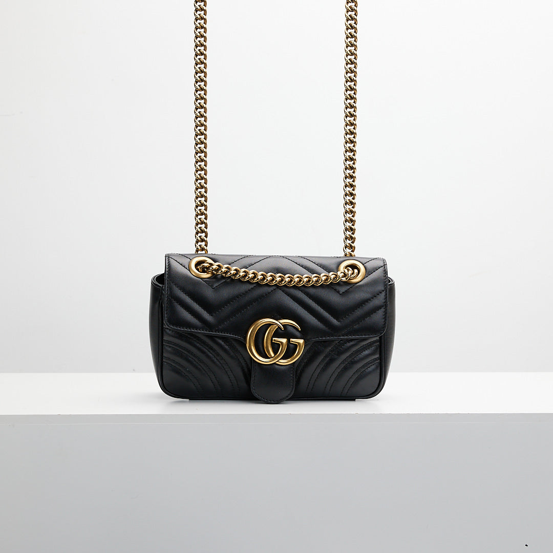 Black quilted handbag with gold chain strap on a light gray background