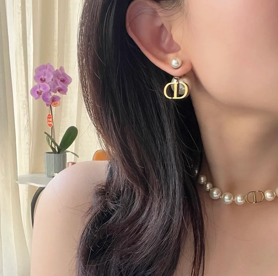A close-up lifestyle shot of a woman wearing a gold-tone double D logo hoop earring with a white pearl stud, along with a matching pearl and gold choker necklace.