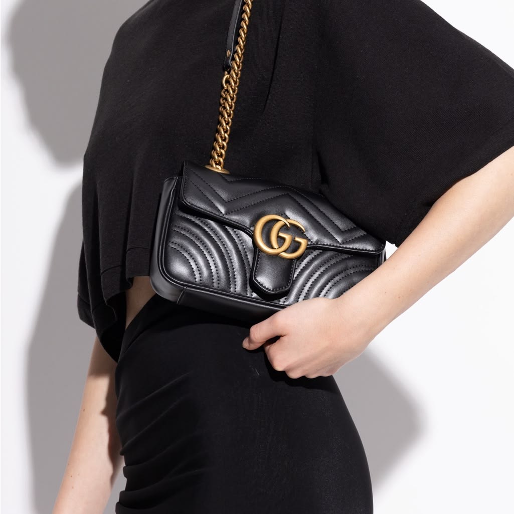 Person holding a black handbag with a gold chain strap against a neutral background