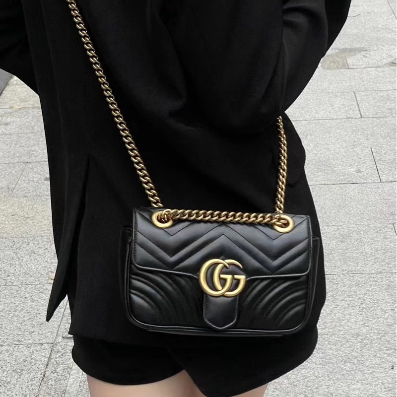Black handbag with gold chain strap held by a person wearing black clothing.