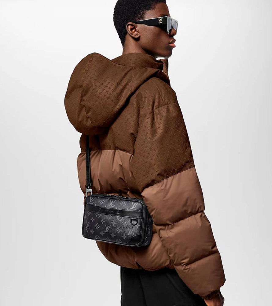 Person wearing a brown puffer jacket with a black patterned bag on a white background