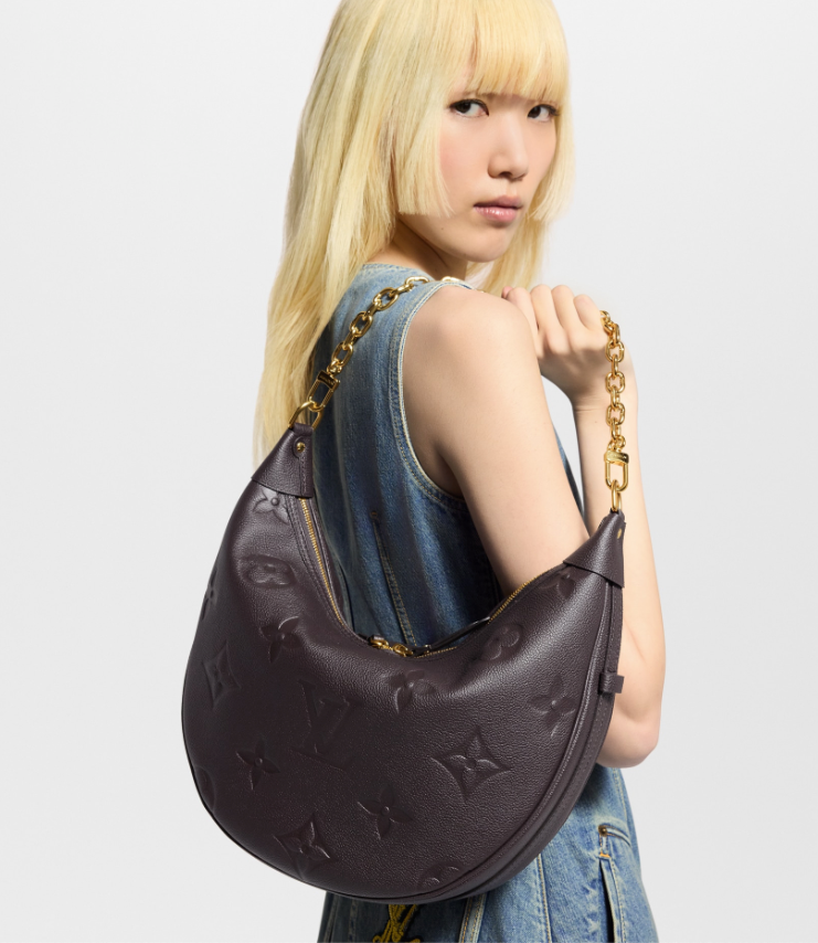 Woman holding a brown handbag with a gold chain strap against a light gray background