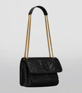 Black handbag with gold chain strap on a light gray background