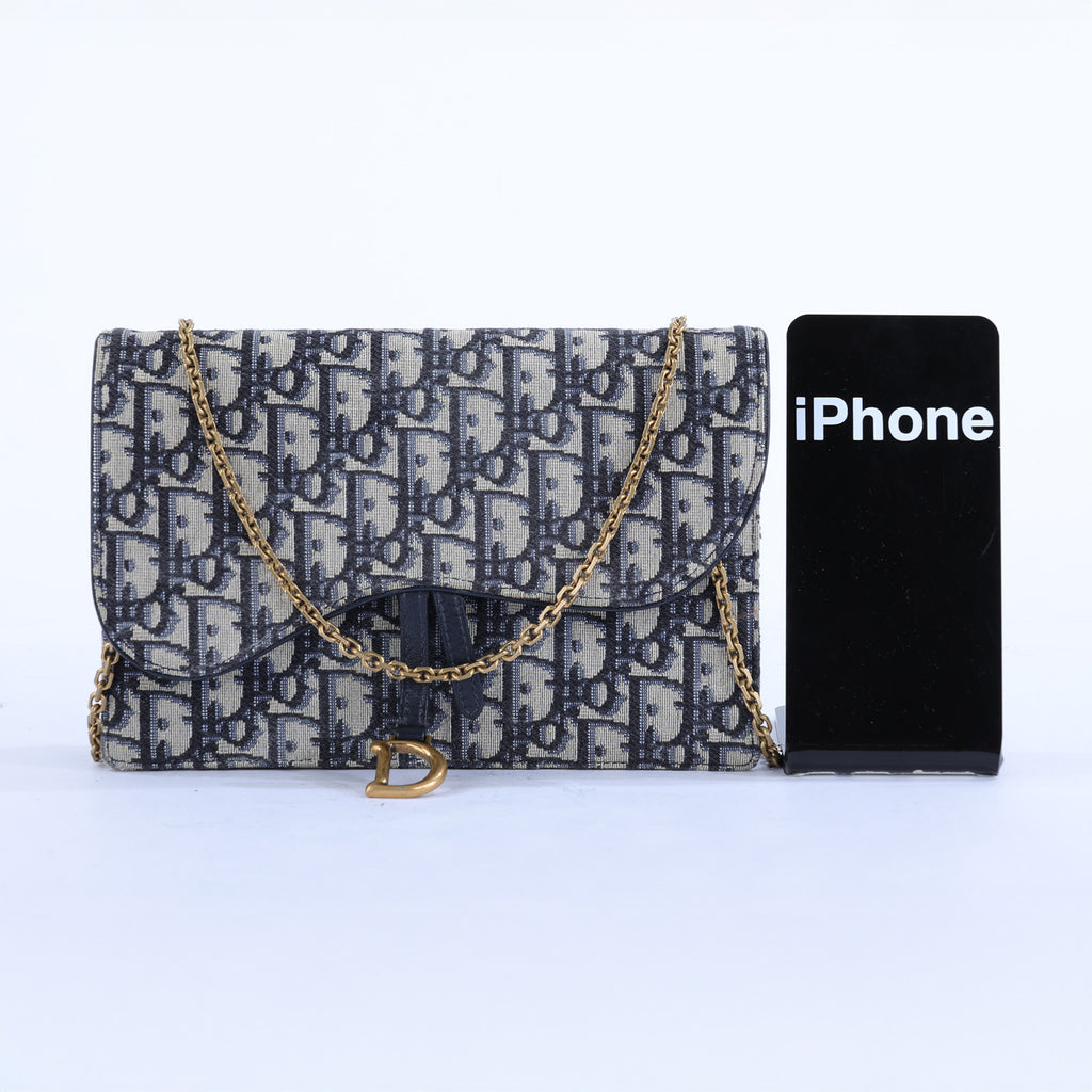 Vintage Jacquard flap shoulder bag in navy and beige monogram canvas with a gold chain strap, shown next to a black smartphone for scale on a white background.