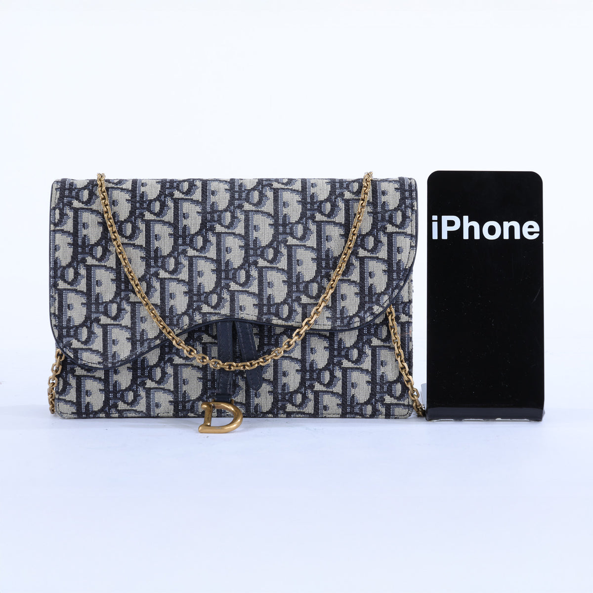 Vintage Jacquard flap shoulder bag in navy and beige monogram canvas with a gold chain strap, shown next to a black smartphone for scale on a white background.
