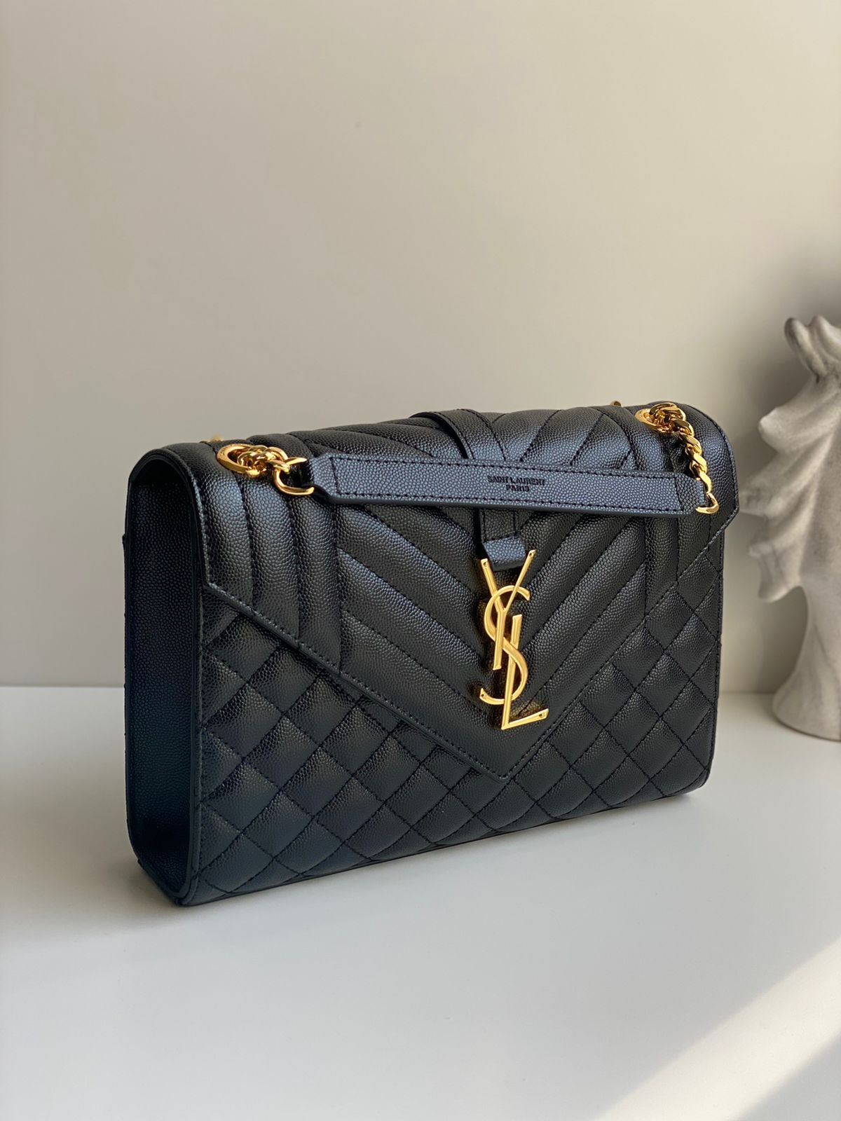 Black quilted envelope chain wallet with matte black logo and gold chain strap, structured evening bag