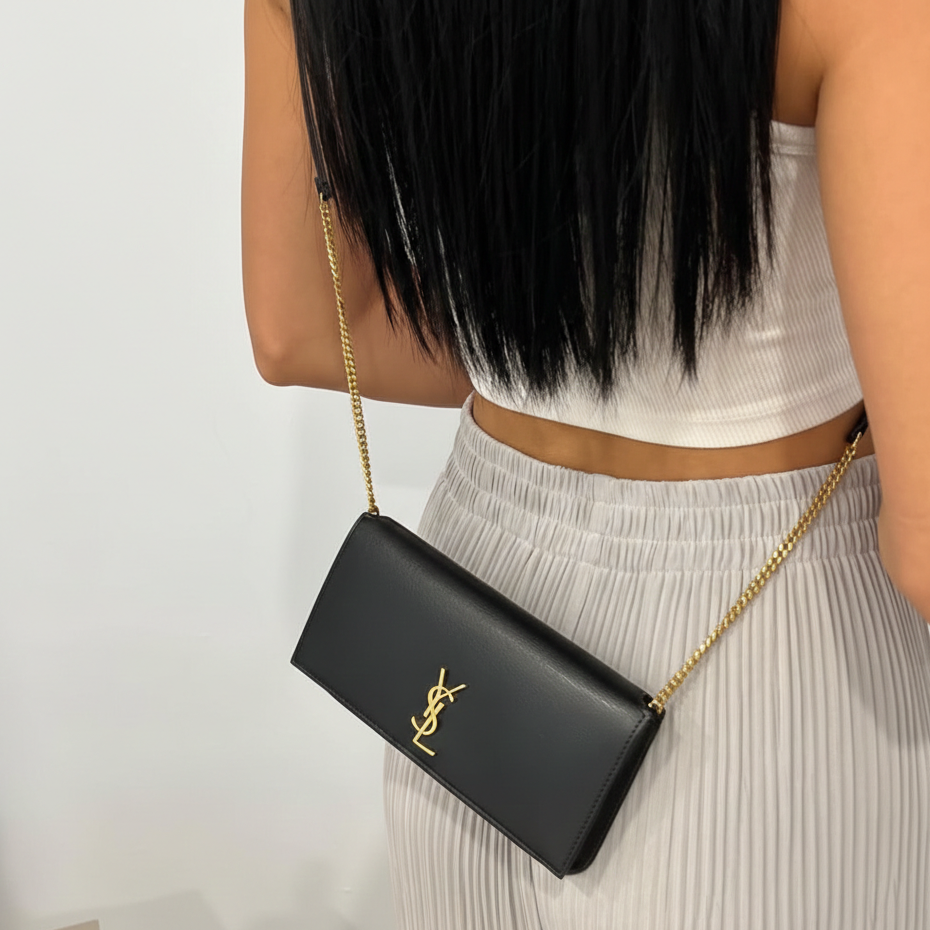 Woman wearing black vertical phone bag with gold chain strap, minimalist clean girl aesthetic outfit.
