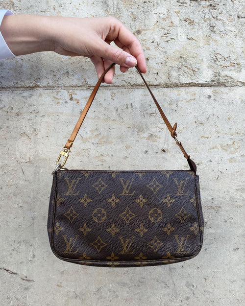 Hand holding a brown monogram handbag against a textured wall.