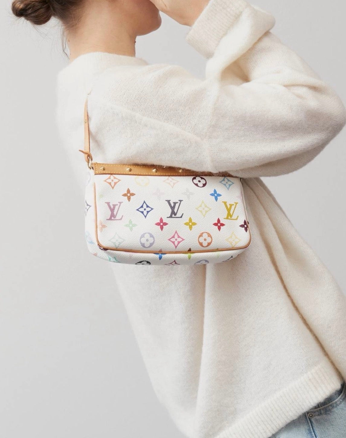 A person wearing a cream knit sweater carries a multicolour shoulder bag with a  tan leather trim