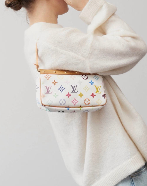 A person wearing a cream knit sweater carries a multicolour shoulder bag with a  tan leather trim