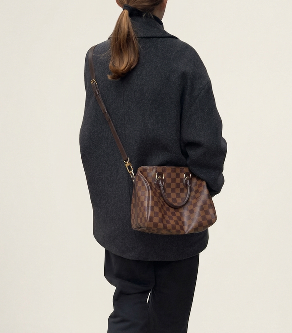 Person wearing a dark outfit with a brown patterned handbag on a plain background