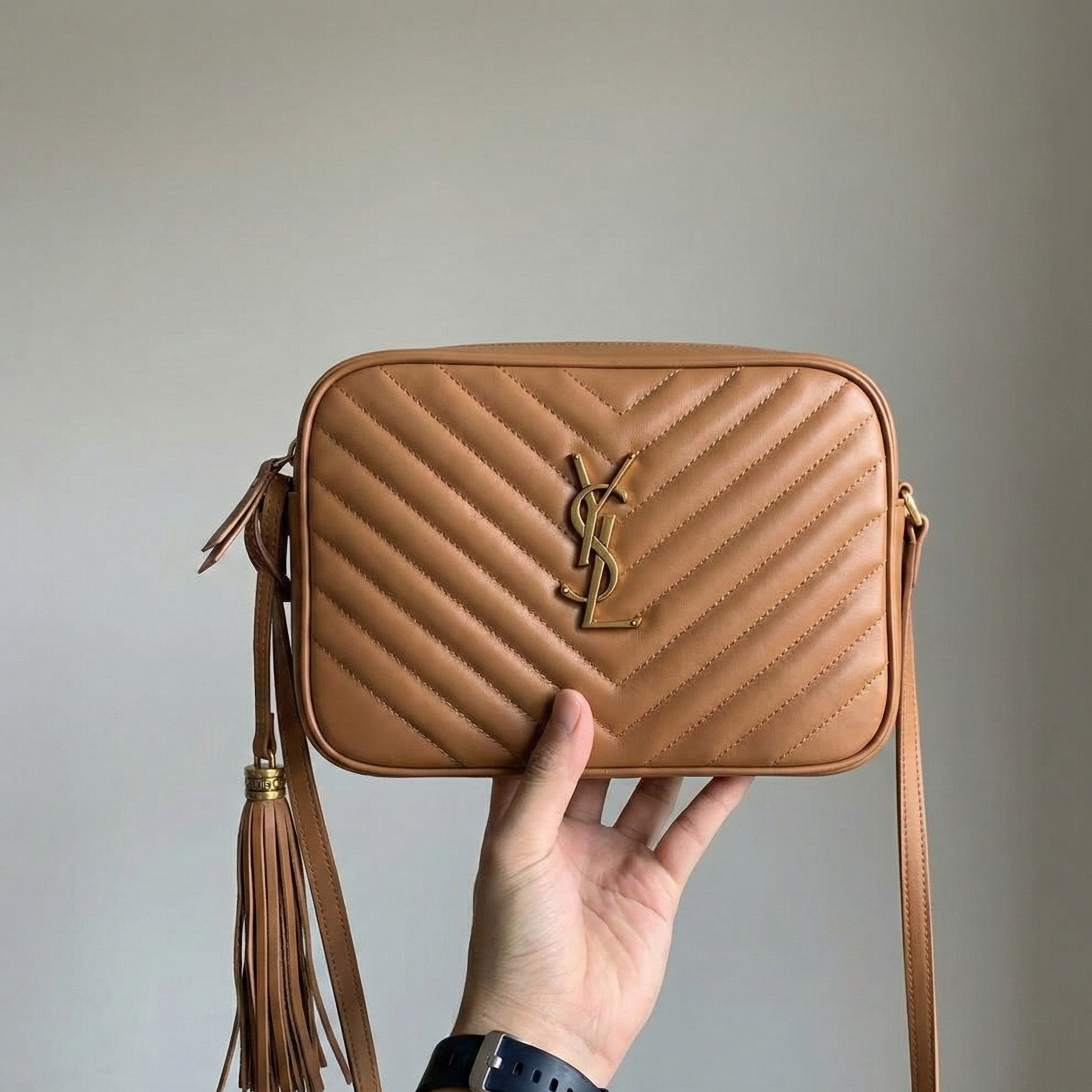 Close up of gold tone zipper and chevron stitching on tan crossbody bag.