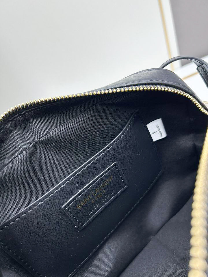 Close up of black chevron quilted texture and gold interlocking hardware on camera bag with leather tassel.