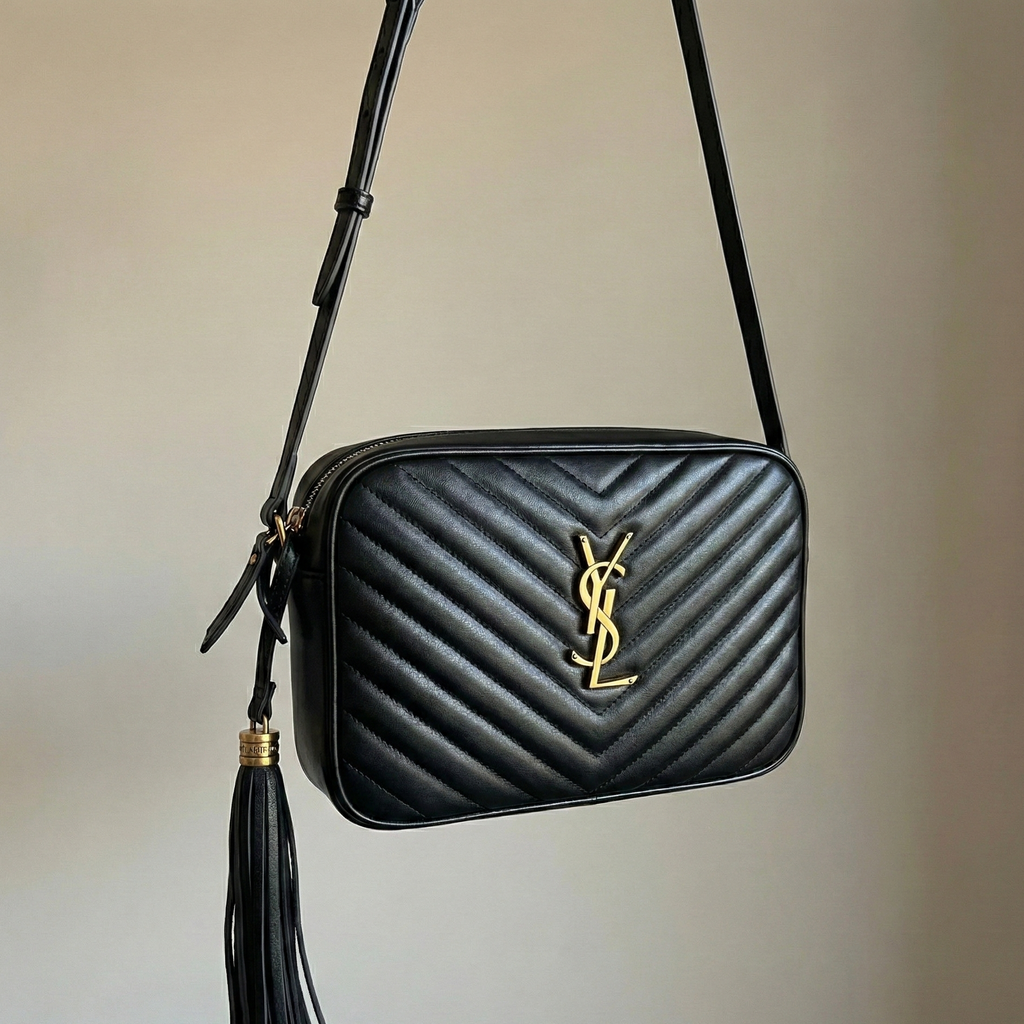 Close up of black chevron quilted texture and gold interlocking hardware on camera bag with leather tassel.