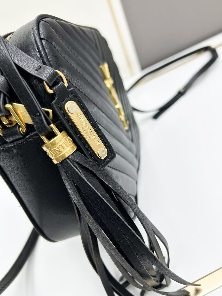 Close up of black chevron quilted texture and gold interlocking hardware on camera bag with leather tassel.