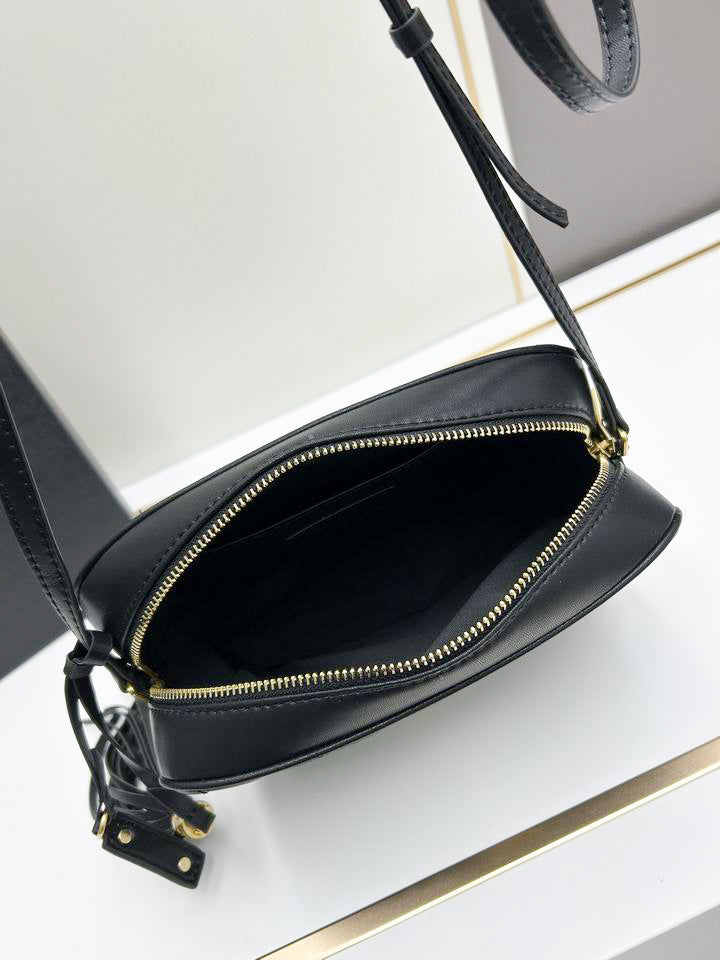 Close up of black chevron quilted texture and gold interlocking hardware on camera bag with leather tassel.