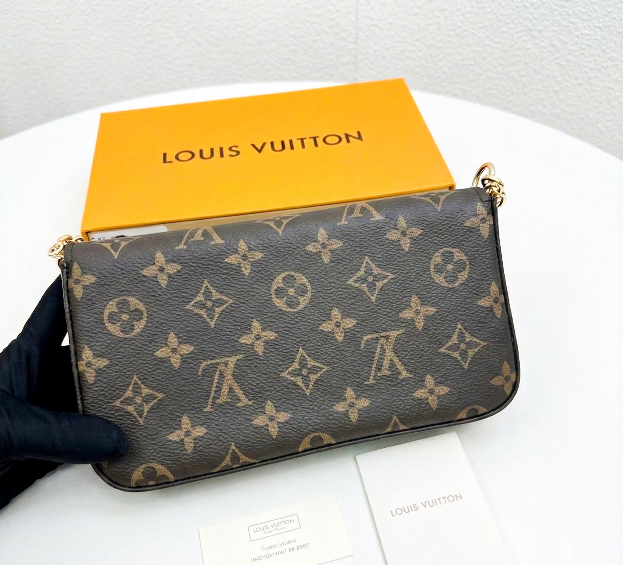 Close up of monogram envelope bag with gold chain strap, accessible luxury handbag