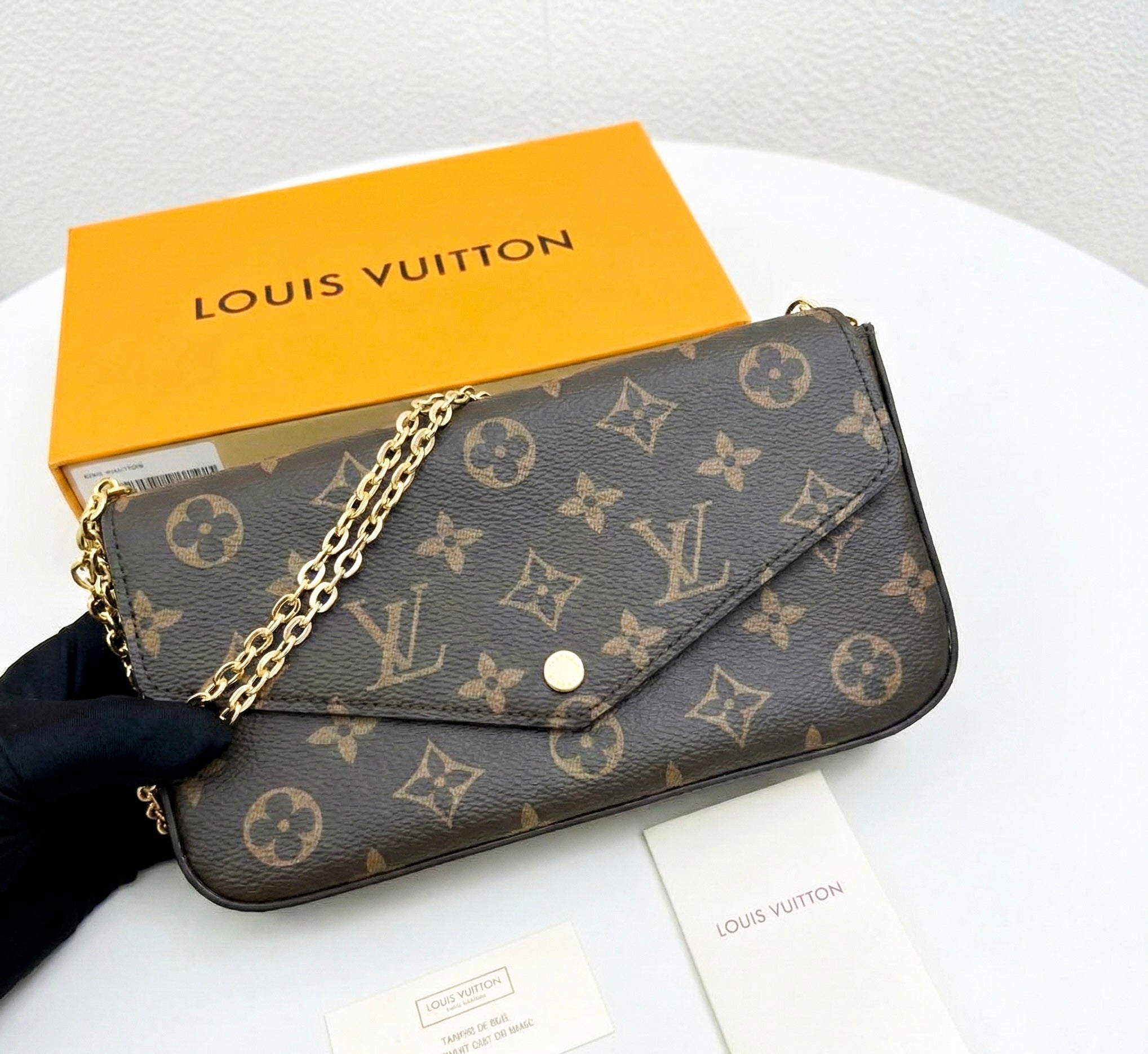 Close up of monogram envelope bag with gold chain strap, accessible luxury handbag.