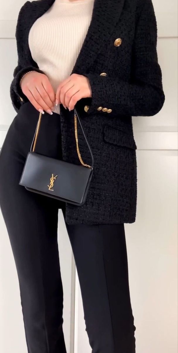 Person wearing a black coat holding a black handbag with gold accents against a white background