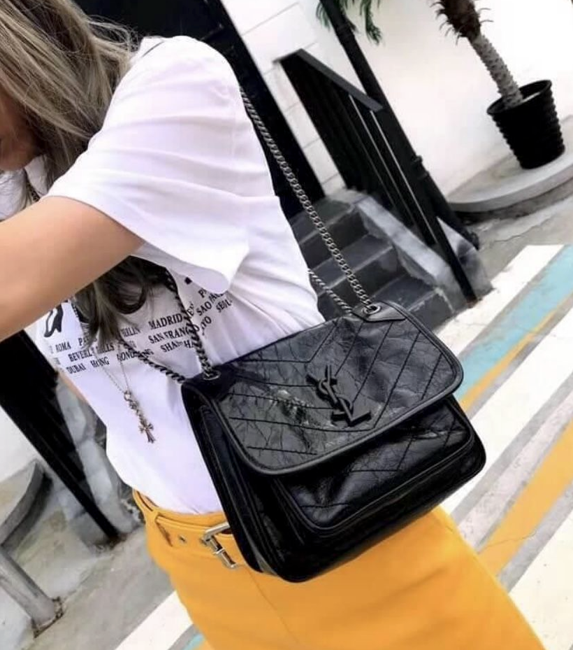 Woman styling a black slouchy flap bag with tonal logo. Cool girl aesthetic outfit with everyday luxury handbag.