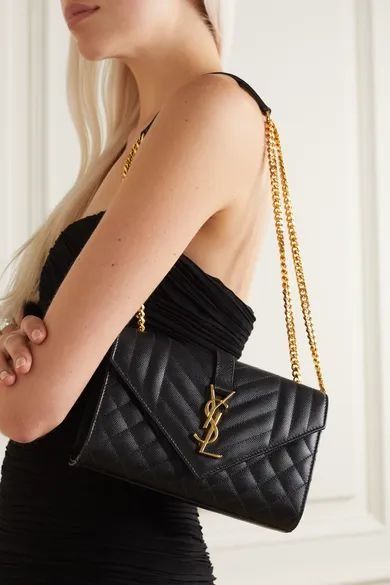 Black quilted handbag with gold chain strap worn by a person in a black outfit.