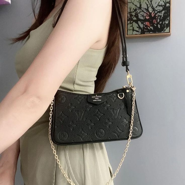 Black handbag with gold chain strap held by a person against a neutral background