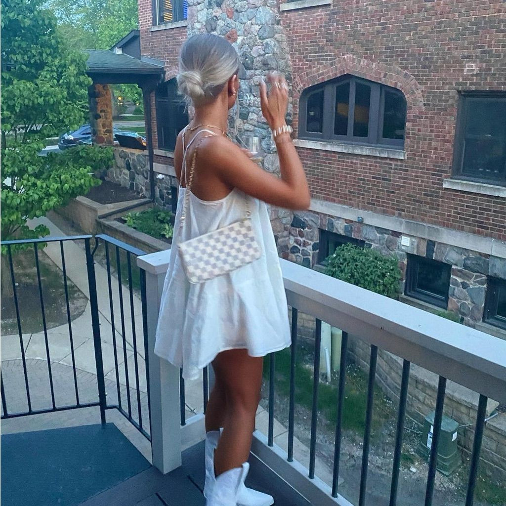 Woman in a white dress standing on a balcony with a checkered bag.