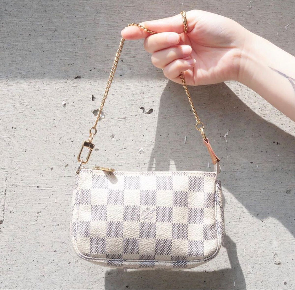 Hand holding a checkered handbag with a chain strap against a concrete wall.