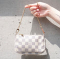 Hand holding a checkered handbag with a chain strap against a concrete wall.